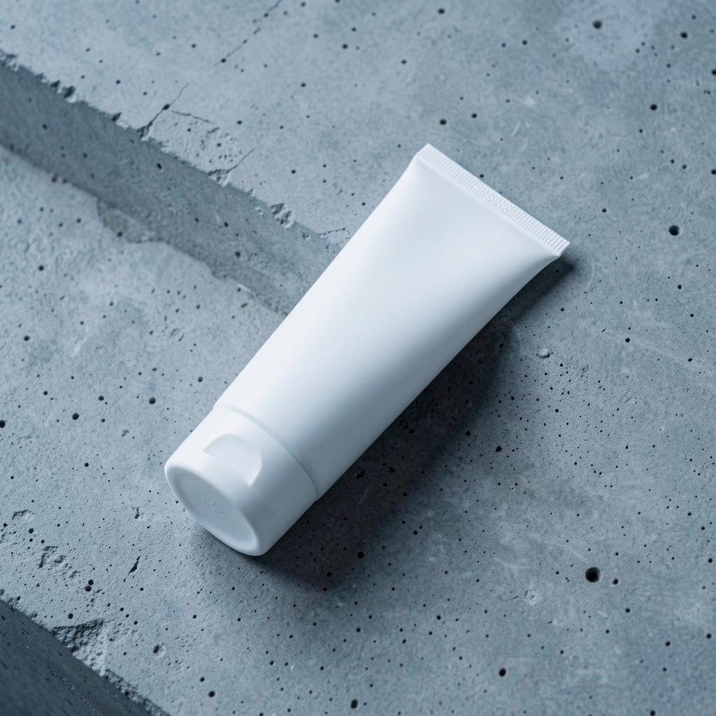 Minimal white tube of body moisturiser lying diagonally on a raw concrete surface, editorial product photography with cool ambient light