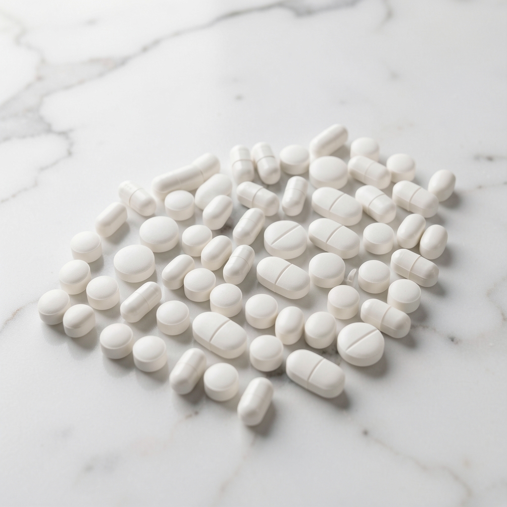 Small white supplement capsules arranged in precise rows on a white marble surface, minimal editorial photography with soft natural light