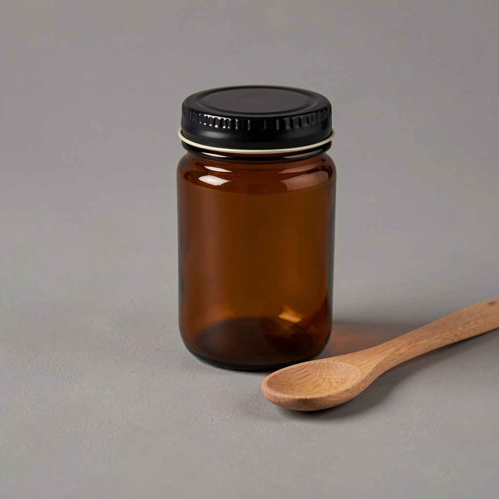 Brown glass supplement jar with black metal lid resting beside a small wooden spoon on a neutral grey surface, warm studio editorial photograph